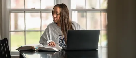 student at laptop, glancing aside at notes